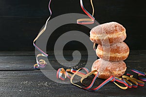 Stacked Berliner doughnuts or Krapfen and some party streamers against a dark rustic background, often served on New Year and