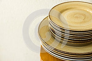 Stacked brown speckled glazed earthenware ceramic plates dishes on wooden table. White wall background. Mediterranean kitchen