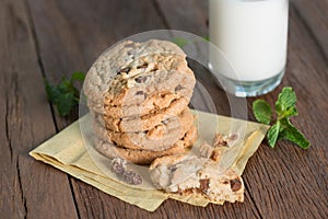 Stacked chocolate chip cookies with milk glass on wooden table.