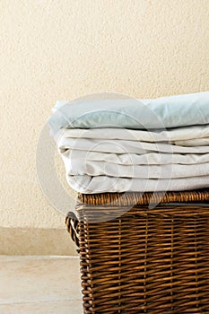 Stacked clean folded cotton bedlinen on wicker chest white wall background. Laundry cleanliness concept. Provence Mediterranean