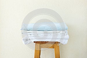 Stacked clean folded cotton bedlinen on wooden stool white wall background. Laundry washing cleanliness concept