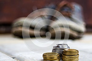 Stacked coins on blurred background of a pair of dirty old boots.