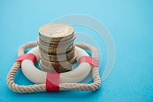 Stacked coins in red lifebuoy or lifebelt with blue background copy space. Assets wealth, money saving