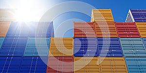 Stacked industrial intermodal cargo transport or shipping containers storage outside with blue sky and sun