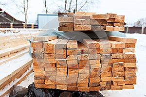 Stacked lumber at construction site. Winter construction of timber house