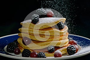 Stacked pancakes with summer berries and falling confectioners sugar