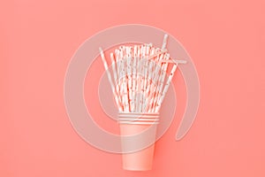 Stacked Pink Drinking Paper Cups with Striped Straws on Trendy Living Coral Color Background. Flat Lay Composition