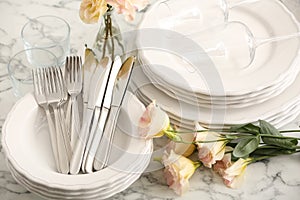 Stacked plates, cutlery and flowers on white marble table, closeup