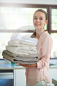 Stacked and ready to pack. Portrait of a young woman holding a pile of folded towels.