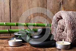 Stacked spa stones, bamboo, candles and towel on wooden table. Space for text