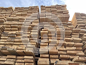 Stacked Timber Planks at a Lumberyard Awaiting Transportation. Stacked wooden planks in varying shades of brown at a