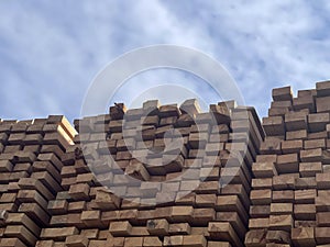 Stacked Timber Planks at a Lumberyard Awaiting Transportation. Stacked wooden planks in varying shades of brown at a