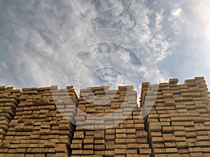 Stacked Timber Planks at a Lumberyard Awaiting Transportation. Stacked wooden planks in varying shades of brown at a