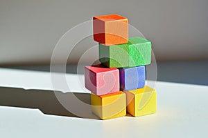 A stacked tower of multi-colored cubes on a light gray surface, with each cube casting a different