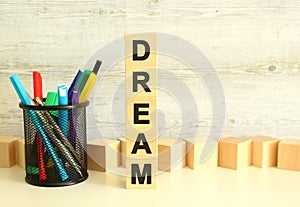 Stacked vertically wooden cubes with letters in the word DREAM on a white work table on a textured gray background.