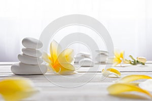 Stacked white stones on white background with yellow frangapani flower