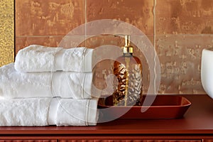 Stacked white towels and soap dispenser on a red surface in front of terracotta tiles.