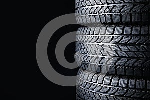 Stacked winter tires on black background, closeup. Space for text