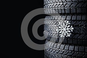 Stacked winter tires with snowflake on black background, closeup. Space for text