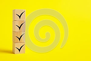 Stacked wooden cubes with check marks on yellow background. Space for text