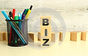 Stacked wooden cubes with letters BIZ on a white work table on a textured gray background.