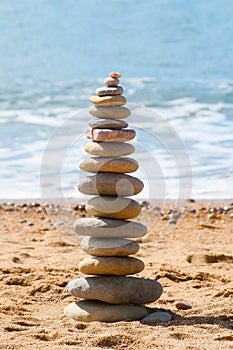 Stacked zen stones on sandy beach with quiet sea waters in background.