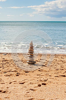 Stacked zen stones on sandy beach with quiet sea waters in background