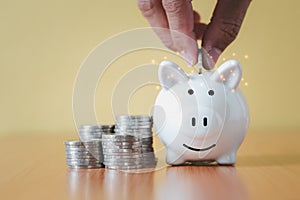 Stacking coins pile and Hand putting coin into white piggy bank for savings with money and planning step up to growing