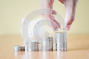 Stacking coins pile and Hand putting coin into white piggy bank for savings with money and planning step up to growing, Saving
