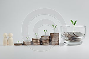 Stacking of money coins, wooden dolls and a glass jar with plants growing on top for business, financial, accounting