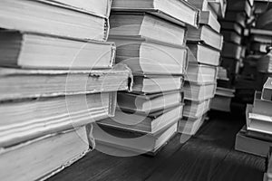 Stacks of books on a wooden table. Black and white photograph of books collected in stacks on the table. Several stacks