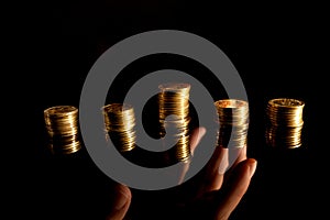 Stacks of coins on the dark background and hand reaching