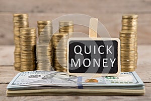 Stacks of coins and dollar bills, blackboard with text QUICK MONEY