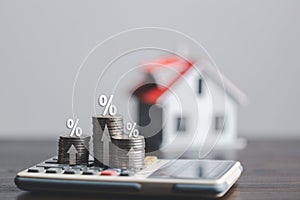 Stacks of coins and model house with percentage symbol for increasing interest rates. Interest rate financial and mortgage rates.