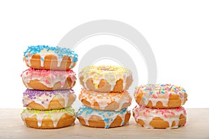 Stacks of colorful frosted candy coated donuts on a light wood table isolated
