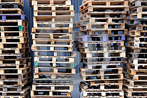 Stacks of colorful rough wooden pallets at warehouse in industrial yard. Pallets background. Cargo and shipping concept