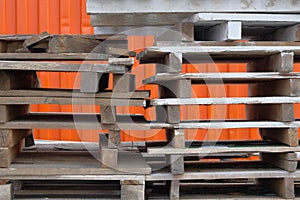 Stacks of colorful rough wooden pallets at warehouse in industrial yard. Pallets on orange background. Cargo and shipping concept