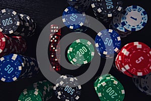 Stacks of different colored poker chips and playing dices on the casino table isolated over black background. Gambling tournament