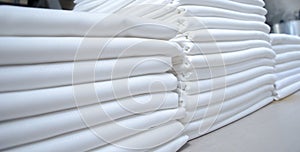 Stacks of folded white fabrics or sheets in an industrial laundry