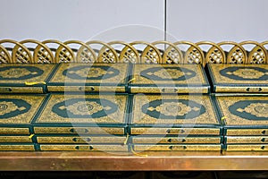 Stacks of green and golden Quran or Quraan books at shelf, closeup detail photo