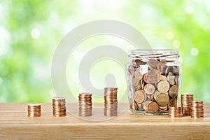 Stacks of money coins and glass jar over green background. Savings, banking, investment, retirement funds or sustainable business