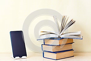 Stacks of old paper books back in the foreground modern digital gadgets mobile phone