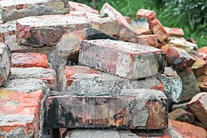 Stacks of old red broken dirty burnt bricks with remnants of cement on grass in garden