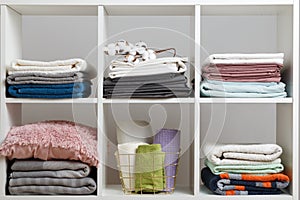 Stacks of towels, sheets, bed linen, blankets and pillows on a white shelf