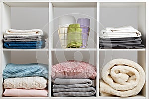 Stacks of towels, sheets, bedding, clothes, blanket and pillow on a white shelf