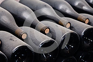 Stacks of wine bottles laying flat in racks in old wine cellar or cave. Concept vault with old rare wines, exclusive