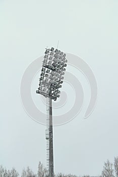 Stadium floodlight with metal pole, lighting mast, tower with floodlights in the sports stadium against the white sky