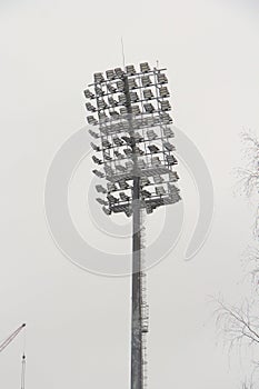 Stadium floodlight with metal pole, lighting mast, tower with floodlights in the sports stadium against the white sky