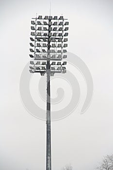 Stadium floodlight with metal pole, lighting mast, tower with floodlights in the sports stadium against the white sky