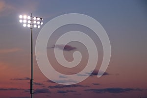 Stadium night lights over football field during sunset with cumulous clouds